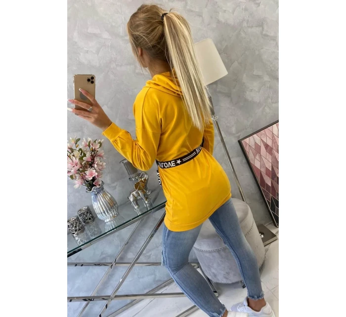 Šaty zdobené stuhou a nápisy v hořčicové barvě