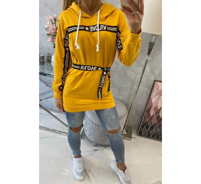 Šaty zdobené stuhou a nápisy v hořčicové barvě