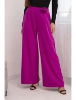 Dámske elegantné nohavice so širokými nohavicami a ozdobným kvetom tmavo fialovej farby Dámske elegantné nohavice so širokými nohavicami a ozdobným kvetom tmavo fialovej farby