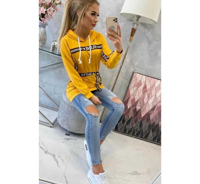 Šaty zdobené stuhou a nápisy v hořčicové barvě